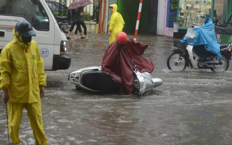 Do lóng ngóng trong chiếc áo mưa tránh đoạn nước ngập sâu và ôtô bên cạnh, một phụ nữ bị ngã ra đường. Ảnh: Tiến Tuấn.