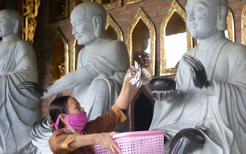 Một người phụ nữ đi thu, gom số tiền lẻ của người dân nhét vào tượng Phật