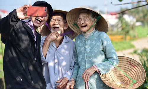 Cụ ông Lê Văn Sẻ, 94 tuổi (trái) và cụ bà Nguyễn Thị Lợi, 88 tuổi chụp ảnh chung với du khách tại vườn rau của nhà, ở làng Trà Quế, xã Cẩm Hà, cách trung tâm phố phổ cổ Hội An 3 km. Ảnh: Media Corp.