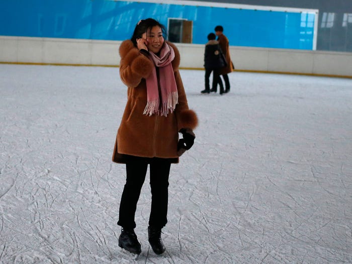 Một phụ nữ Triều Tiên nói chuyện trên điện thoại di động khi cô ấy trượt băng trên sân băng ở Bình Nhưỡng, Triều Tiên. Anh: @AFP.