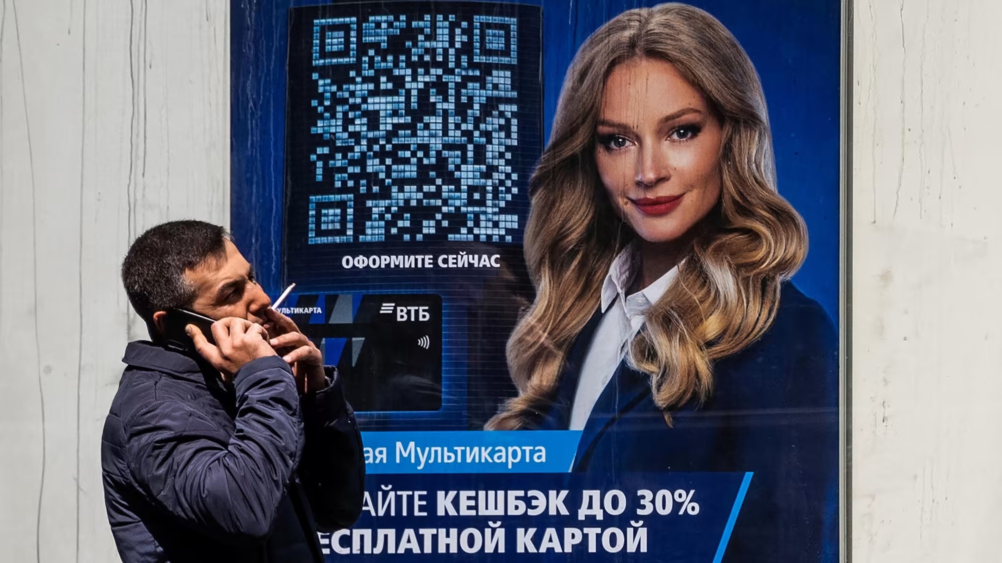 Một người đàn ông nói chuyện với điện thoại di động bên cạnh văn phòng ngân hàng VTB ở Moscow. Các thương hiệu điện thoại thông minh Trung Quốc đã tăng thị phần tại Nga. Ảnh: @AFP.