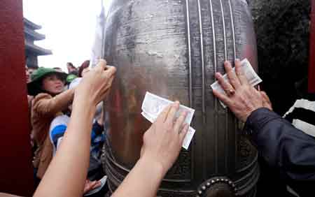 Người hành hương xoa tiền vào chuông ở chùa Yên Tử (Quảng Ninh) để cầu may. 