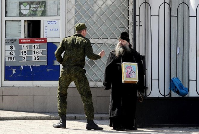 Một người lính Nga nói chuyện với một giáo sĩ Chính thống giáo trước cửa một tổ chức tín dụng ở Simferopol, Crimea (Nguồn: AFP)