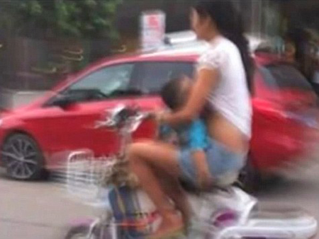 Ảnh chụp bà mẹ trẻ vừa đi xe đạp điện vừa cho con bú trên đường phố Tô Châu, Trung Quốc 