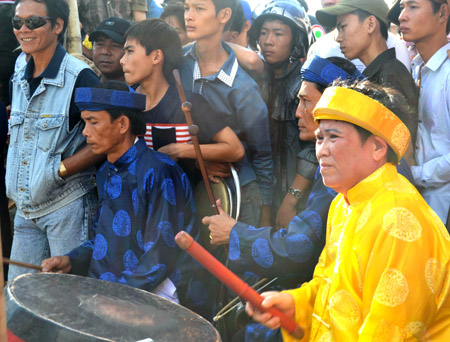 Bà Lê Thị Tá nghiêm trang trong trang phục áo dài, khăn đóng đánh trống chầu tại một buổi hát tuồng