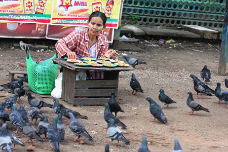 Quầy hàng bán chim bồ câu ở Yangon.  Phía sau người bán hàng ở panô  quảng bá về SEA Games 27. 